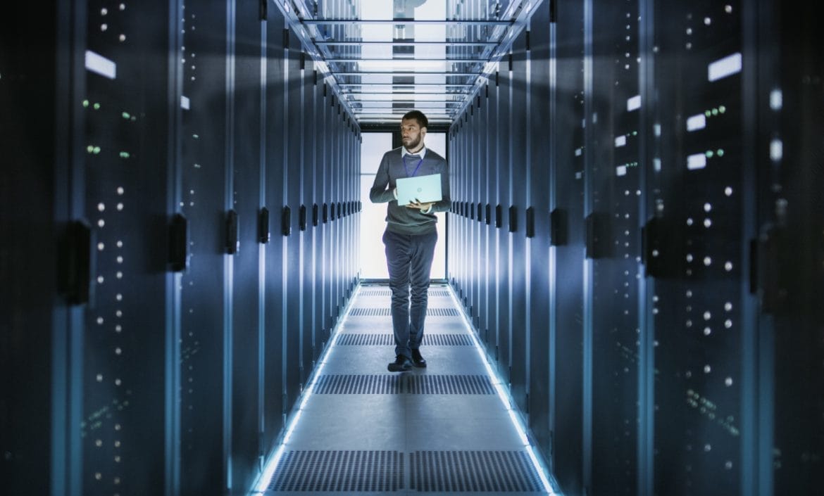 IT Technician Works on Laptop in Big Data Center full of Rack Servers.